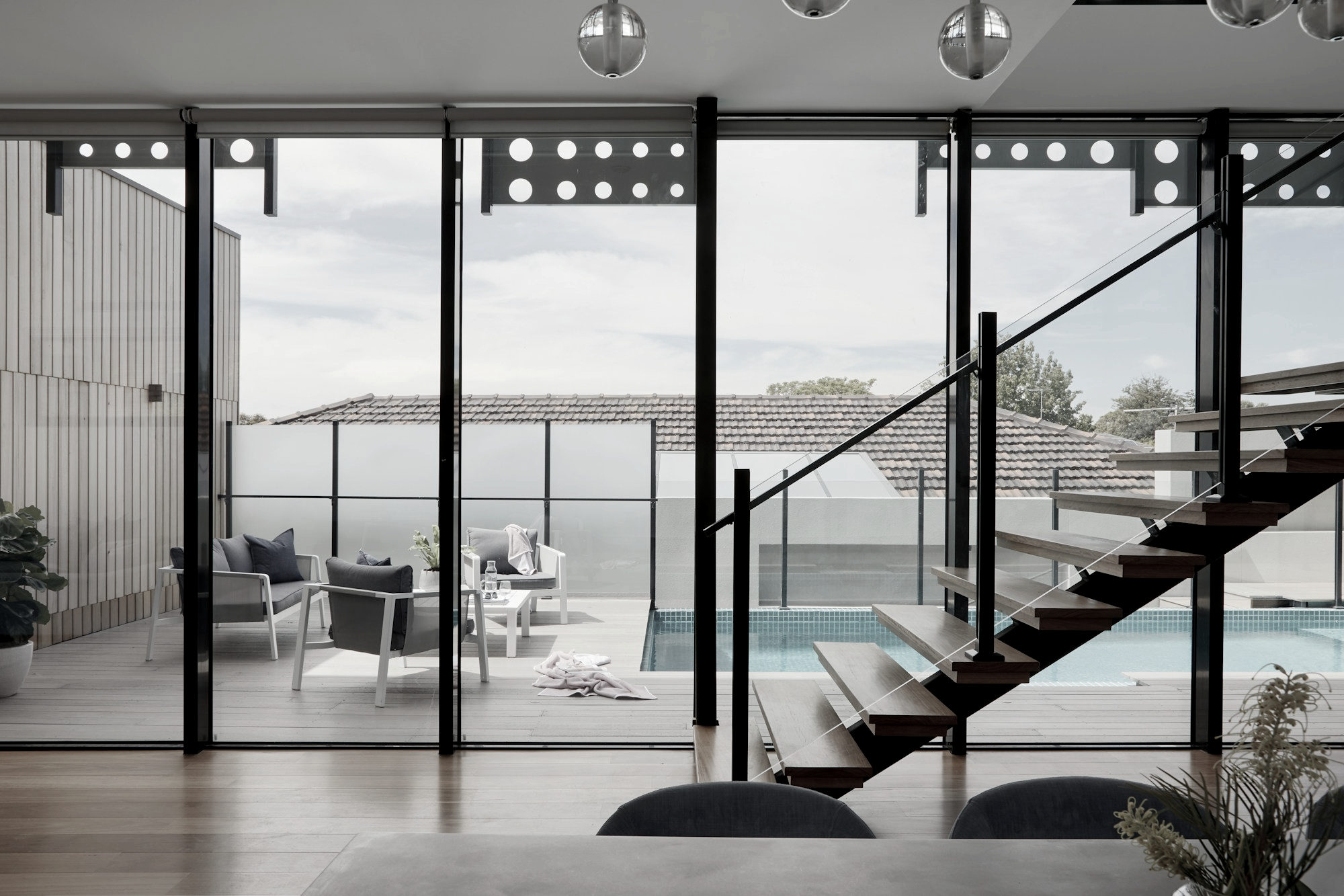 Steel-framed glazing wall with a cantilevered timber stair, looking out to a terrace