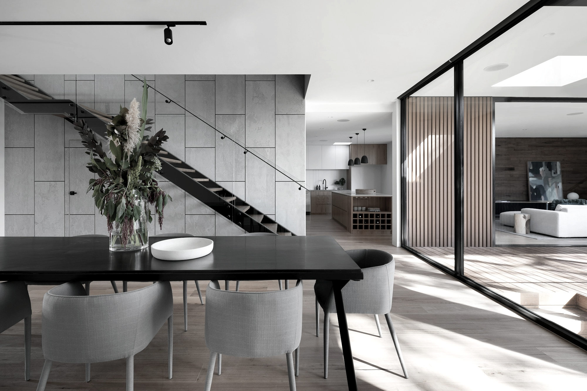 Dining table against a board-formed concrete wall with a steel stair rising behind it